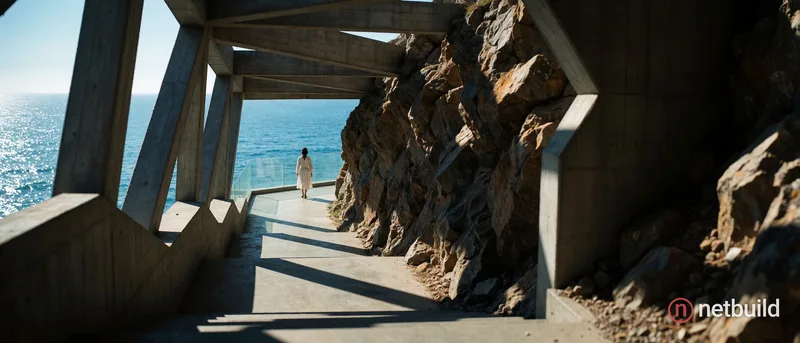 A brutalist concrete corridor descends stark stairs, merging directly into a rugged natural rock cliff on the right. Massive geometric beams cast shar...